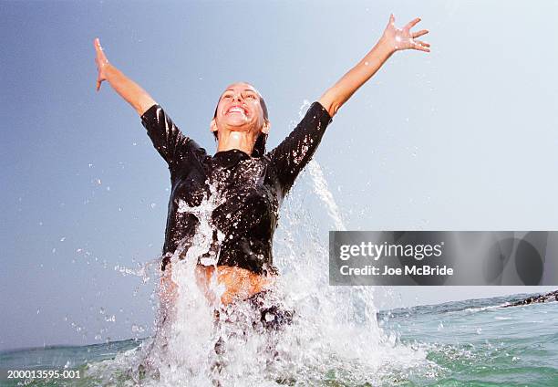 woman emerging from ocean, smiling with arms in air - waist deep in water stock pictures, royalty-free photos & images