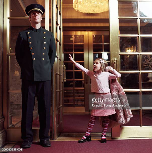 girl (4-6) standing in doorway beside doorman - portiere foto e immagini stock
