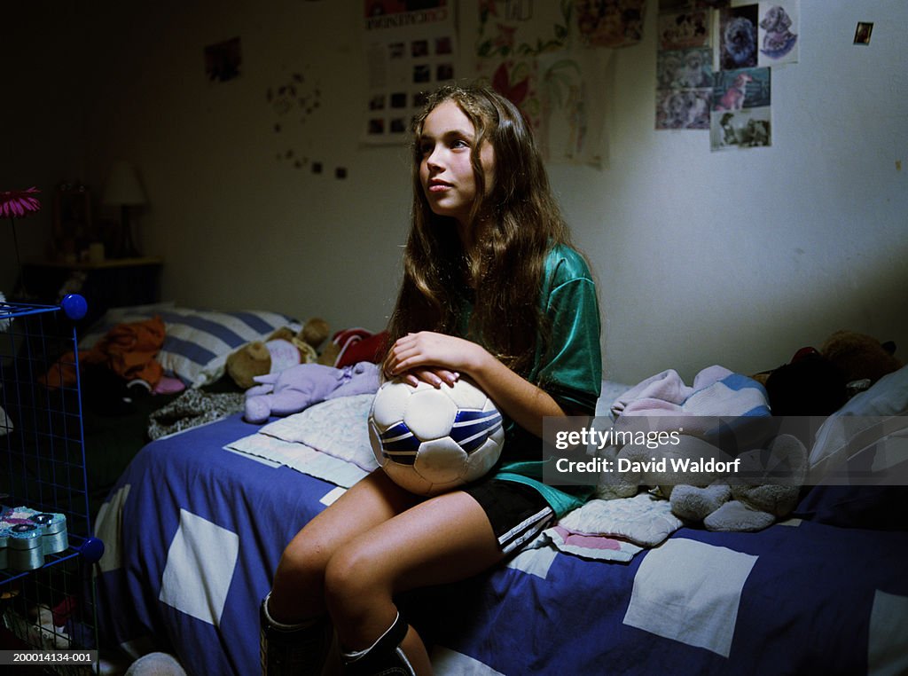 Teenage girl (12-14) sitting on bed with soccer ball