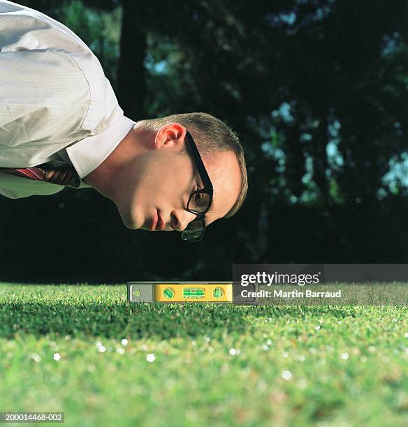businessman using spirit level on lawn, close-up - obsessive stockfoto's en -beelden