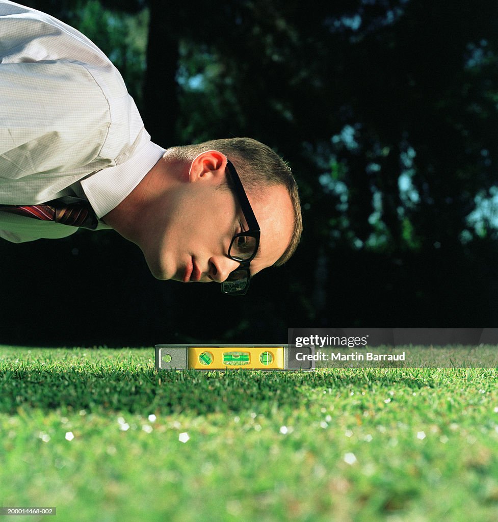 Businessman using spirit level on lawn, close-up