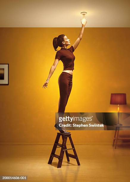 woman standing on stepladder changing light bulb in living room - 手を伸ばす 女性 ストックフォトと画像
