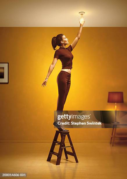 woman standing on stepladder changing light bulb in living room - andar em bico de pés imagens e fotografias de stock