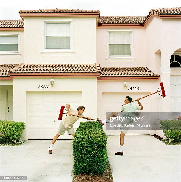 two neighbours fighting with brooms over hedge - vizinho imagens e fotografias de stock