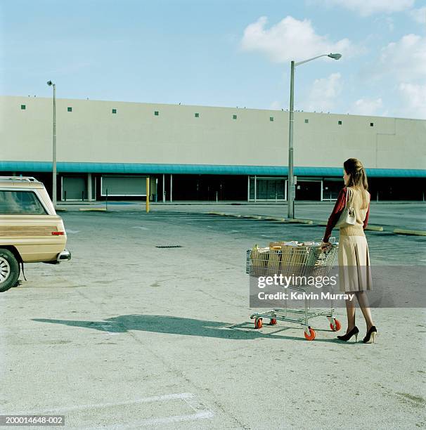 young woman pushing trolly full of groceries in car park - trabalho fastidioso - fotografias e filmes do acervo