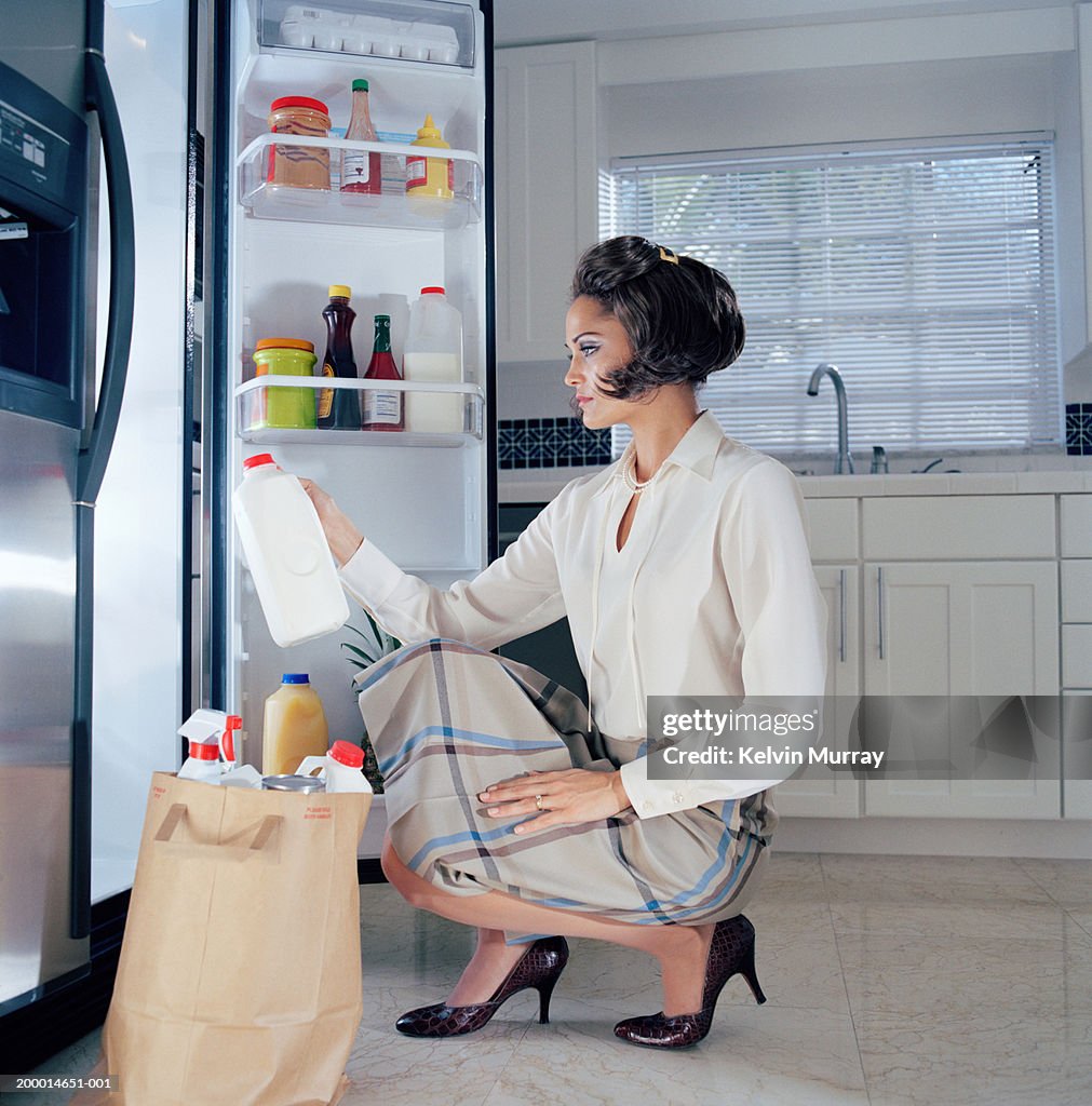 Young woman putting grocery shopping in refrigerator