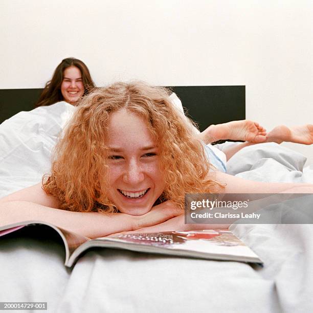 two teenage girls (14-16) on bed (focus on girl with magazine) - barefoot redhead ストックフォトと画像