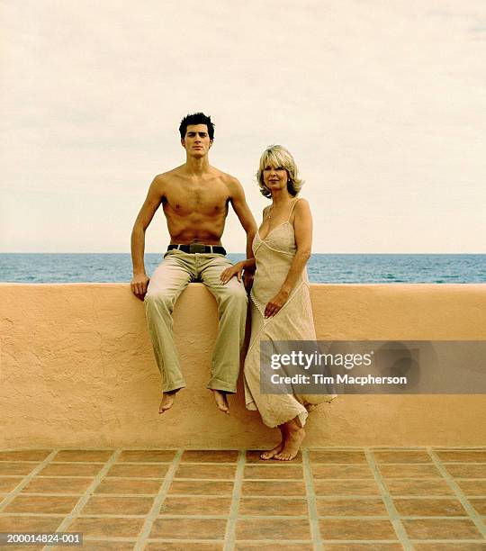 mature woman beside young man sitting on wall, portrait - may december romance stock pictures, royalty-free photos & images