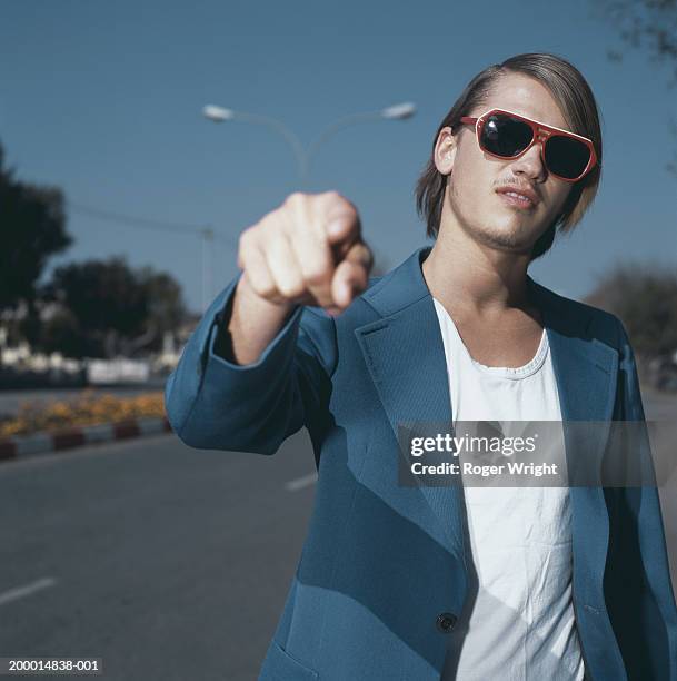 young man in street wearing sunglasses, pointing, close-up - vantarsi foto e immagini stock