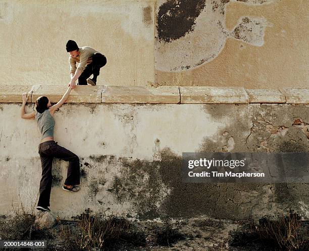 young man helping young woman over wall - klettern stock-fotos und bilder
