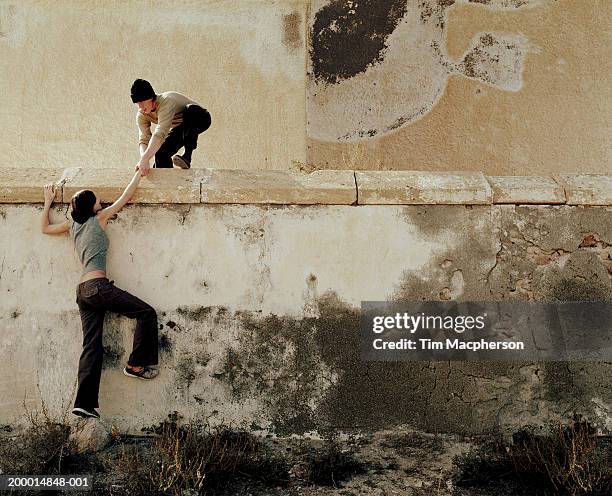 young man helping young woman over wall - person escaping stock pictures, royalty-free photos & images