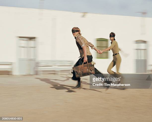 couple in masks running with bag of money (blurred motion) - escape stock pictures, royalty-free photos & images