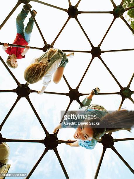 three children (4-13) playing on climbing dome, low angle view - al revés posición descriptiva fotografías e imágenes de stock