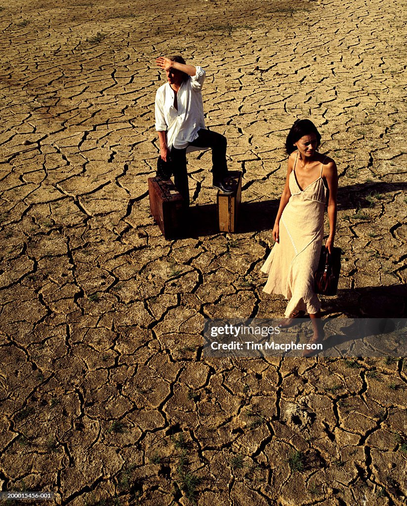 Couple with luggage standing on cracked mud surface