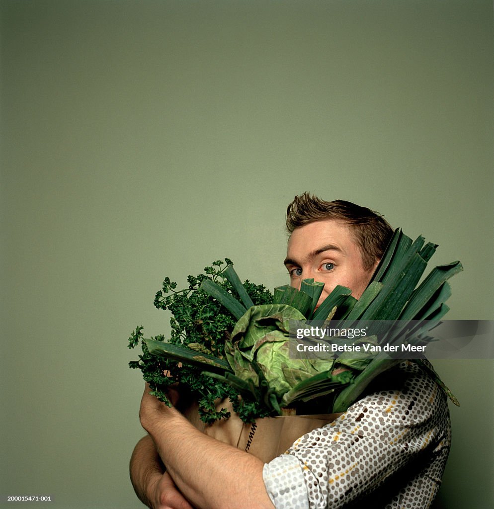 Young man holding bag full of vegetables, portrait