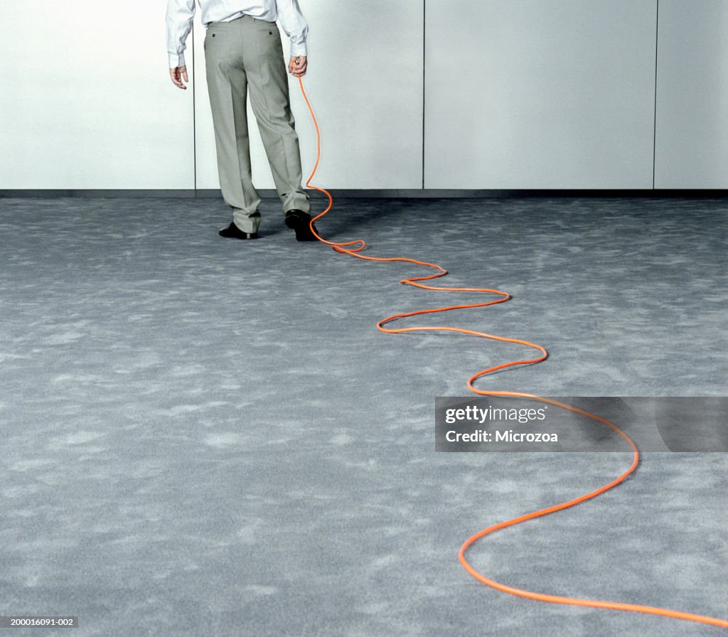 Male executive dragging extension cable across office, low section