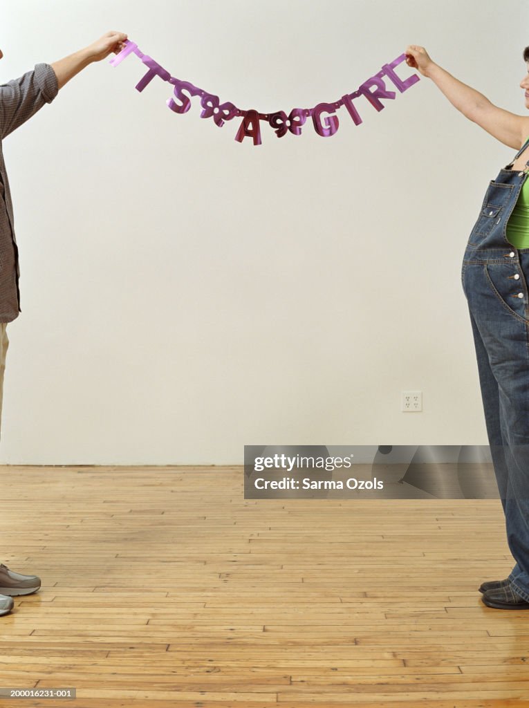 Couple holding up 'It's a girl' sign in apartment