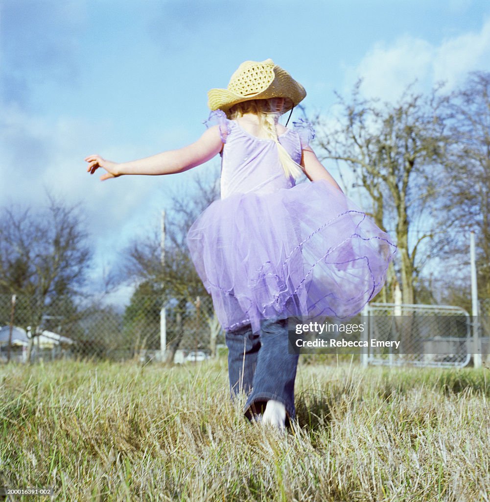 Girl (5-7) playing outside in yard, rear view