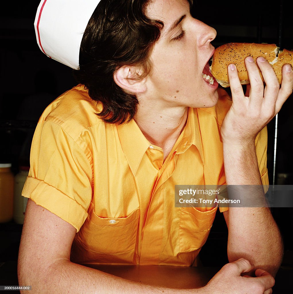 Teenage boy (16-18) in uniform, eating hot dog, close up
