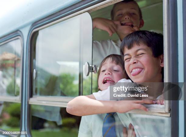 three boys (6-9) poking tongues out, view through school bus window - out bus window stock pictures, royalty-free photos & images