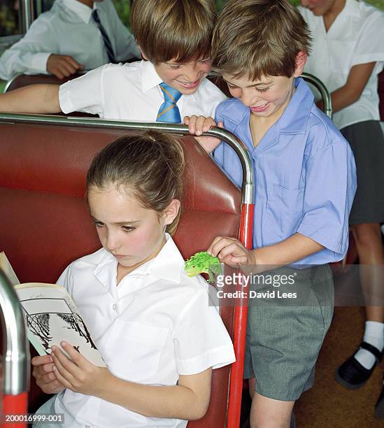 children (6-10) on school bus, boy placing toy frog on girl's shoulder - young girl reading book bus foto e immagini stock