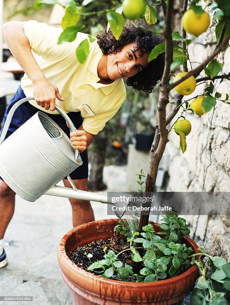 Teenage boy (15-17) leaning over to water plant, smiling