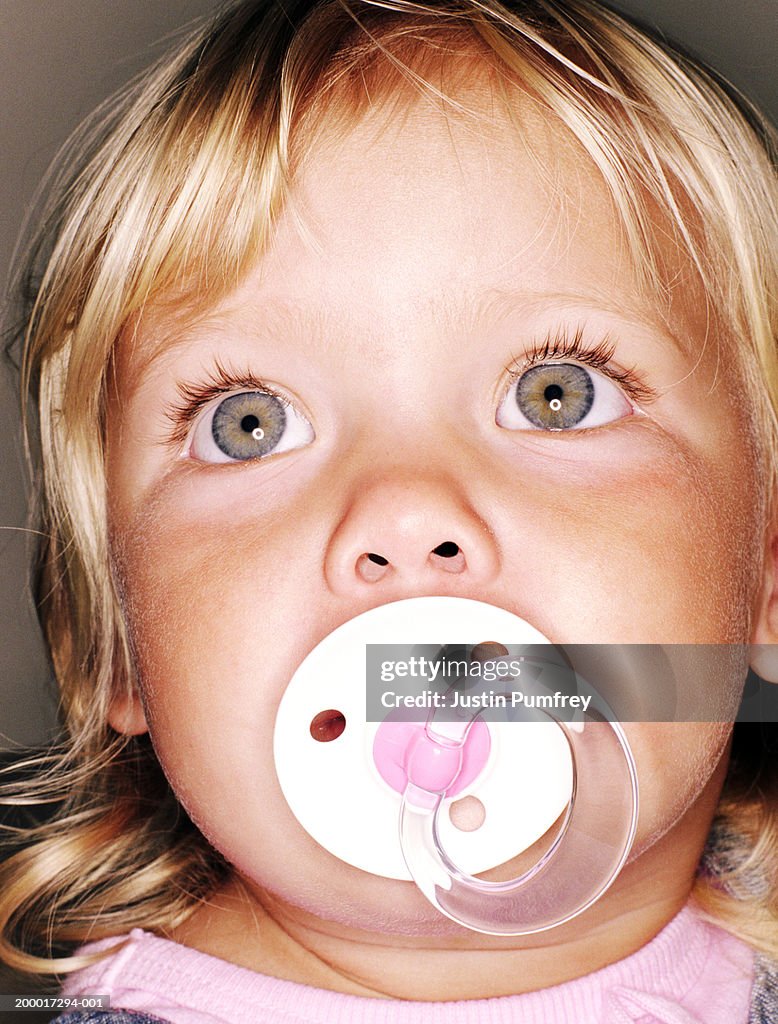 Baby girl (18-21 months) with dummy in mouth looking upwards, close-up