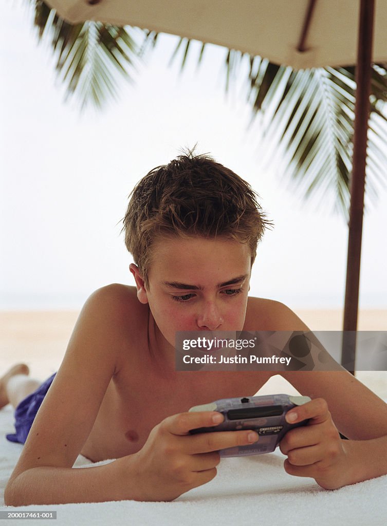 Teenage boy (12-14) lying on sun lounger playing electronic game