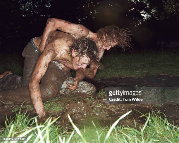 two young men wrestling in mud - ringen stock-fotos und bilder
