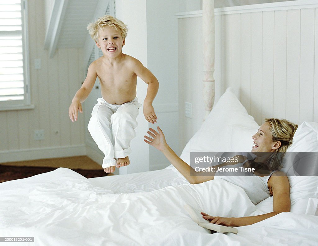 Boy (3-5) jumping on bed beside mother