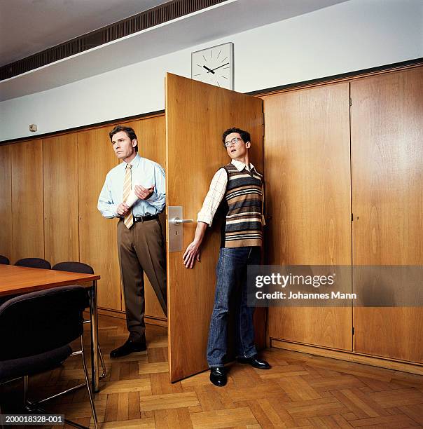 businessman entering room, young man hiding behind door - cower stock pictures, royalty-free photos & images