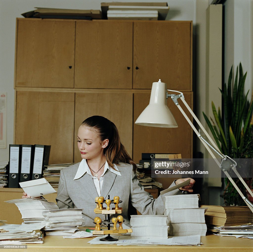 Teenage girl (15-17) working in office,  piles of envelopes on desk