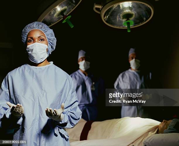 female surgeon wearing scrubs, surgeons and patient in background - portrait professional dark background stock-fotos und bilder