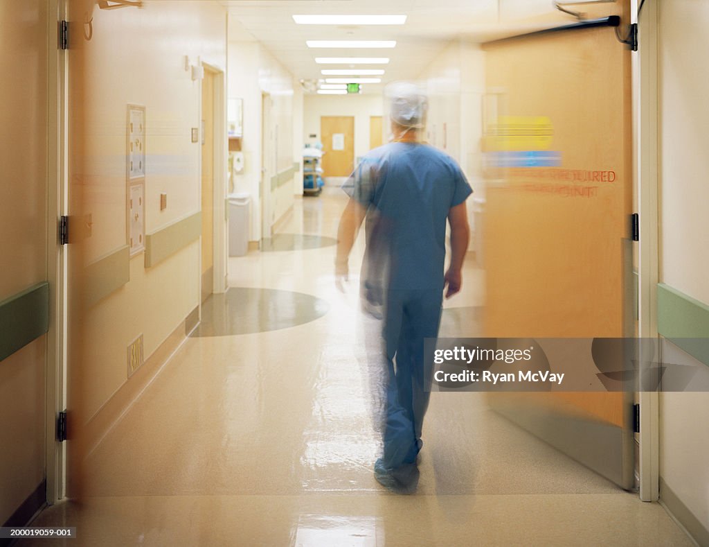 Male surgeon walking down corridor, rear view (blurred motion)