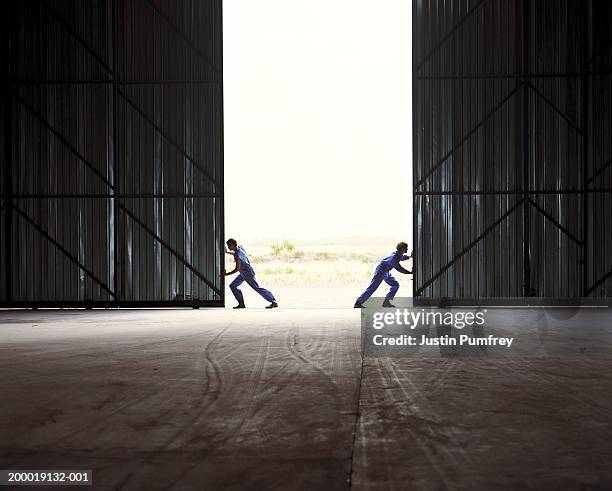 two men opening warehouse doors - hangar stock pictures, royalty-free photos & images