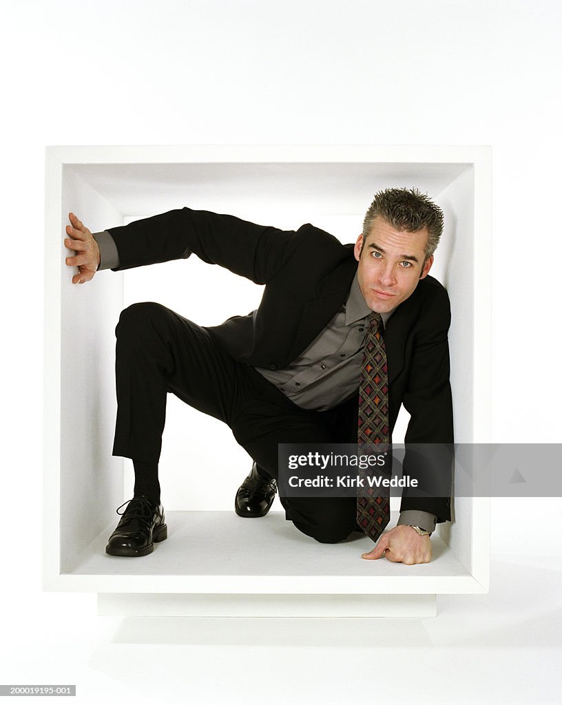 Businessman crouching within white box