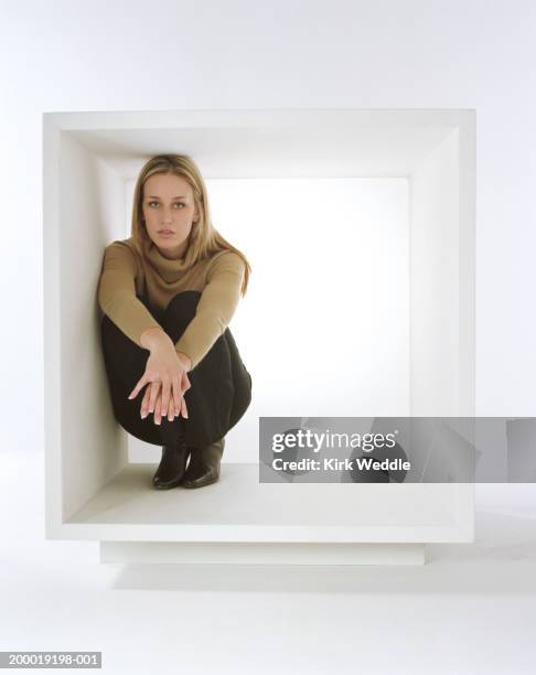 young woman crouching inside white box - atrapado descripción física fotografías e imágenes de stock