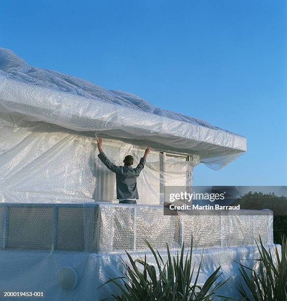 young man wrapping house in bubble pack - avvolto foto e immagini stock