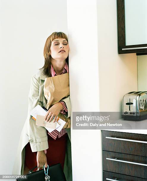 young woman holding post and bags leaning against wall, eyes closed - ankommen stock-fotos und bilder
