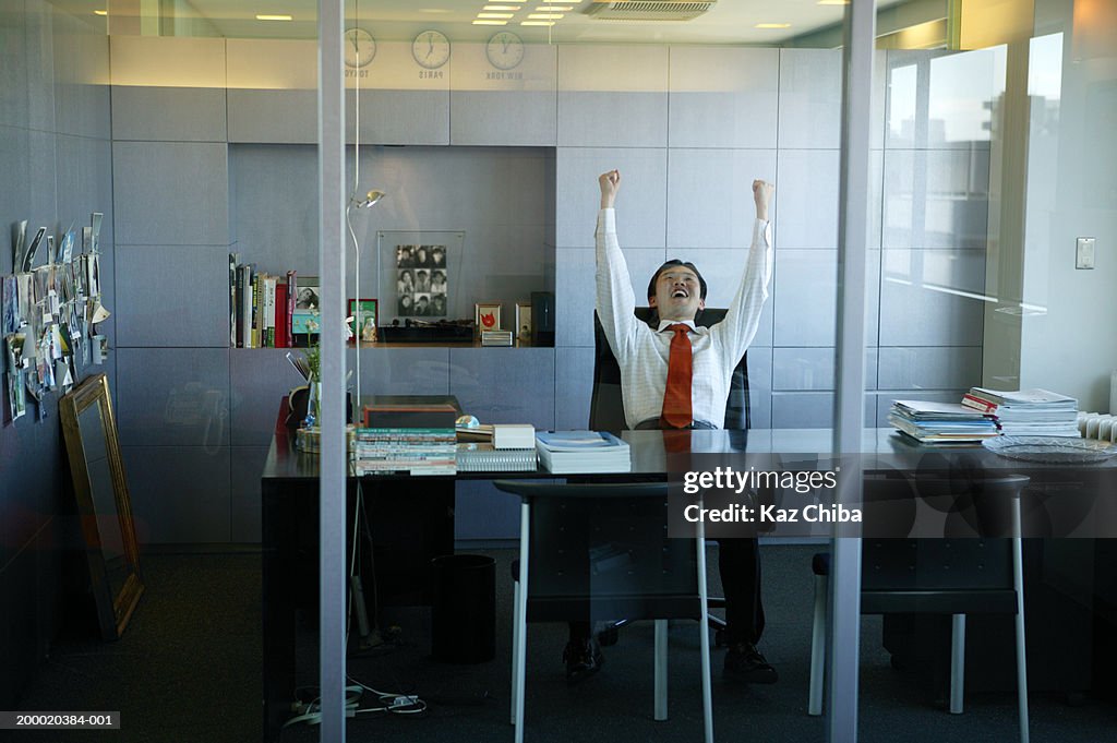Businessman at desk, with arms in the air smiling