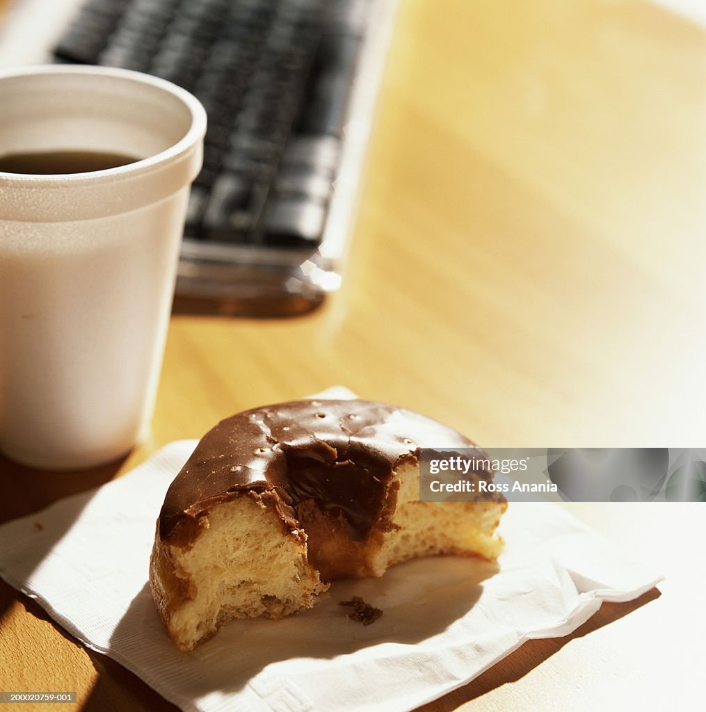 Half eaten chocolate-covered doughnut beside cup of coffee