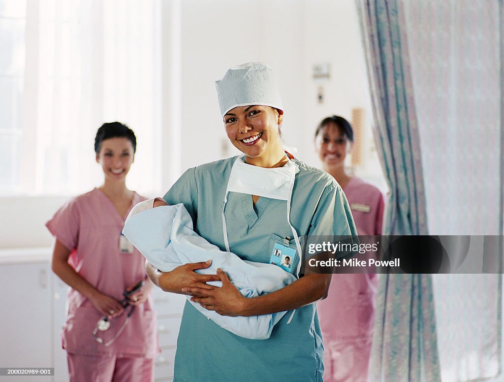 Delivery room nurse holding baby, nurses in background