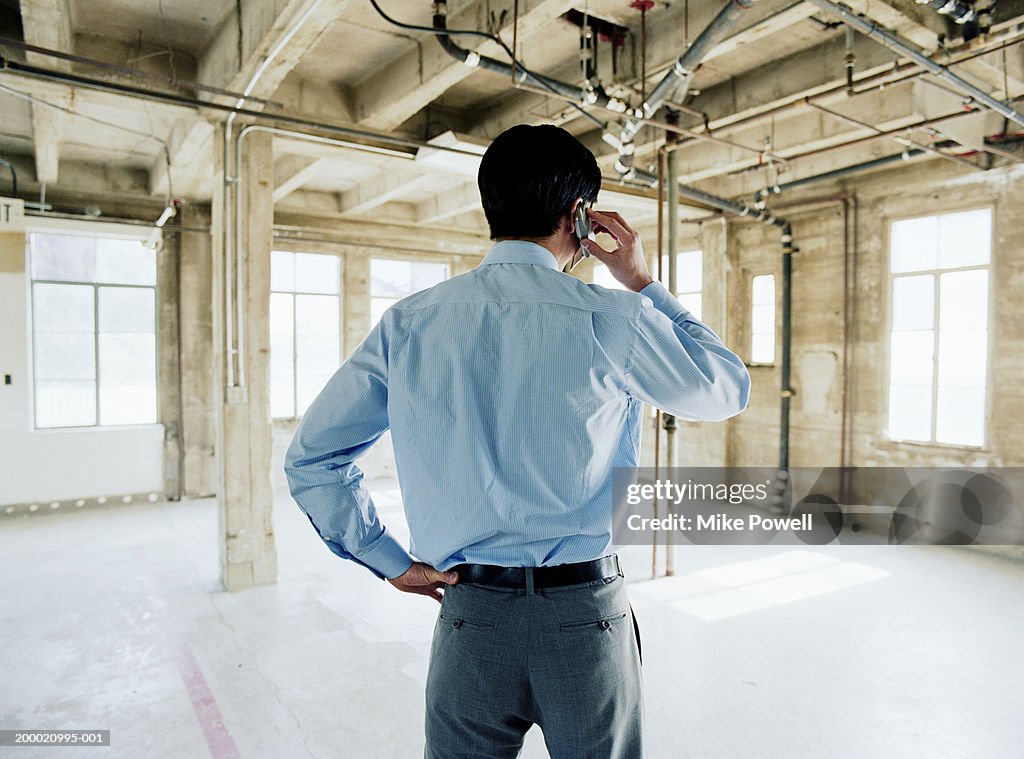 Businessman using mobile phone in empty office space, rear view