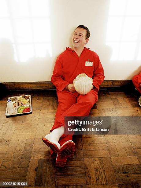 man wearing boiler suit sitting against wall, laughing - red jumpsuit stock pictures, royalty-free photos & images