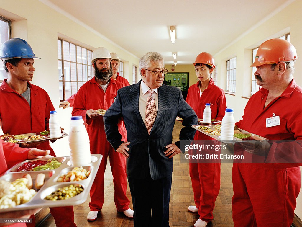 Mature businessman standing with workmen carrying trays of food