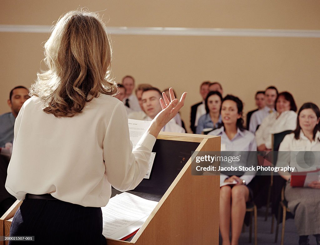 Businesswoman at podium addressing colleagues, rear view