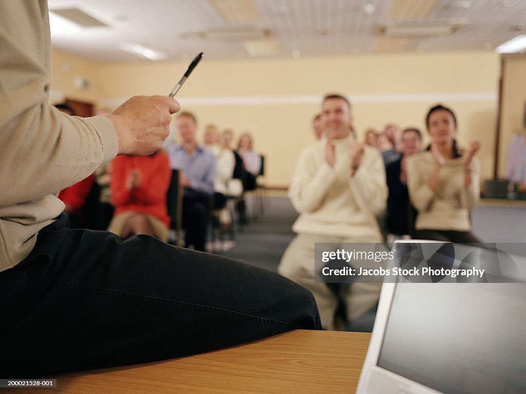 Businessman sitting on desk addressing colleagues, rear view, close-up