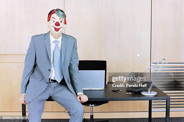 businessman sitting at edge of desk wearing clown mask - kantoorclown stockfoto's en -beelden