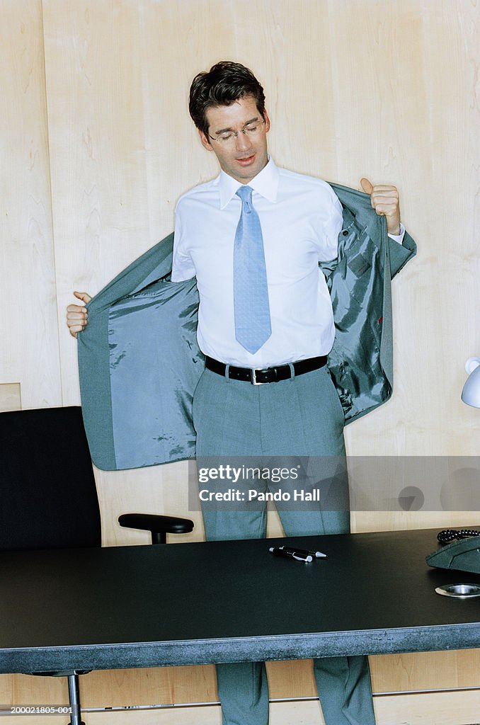 Businessman behind desk removing suit jacket