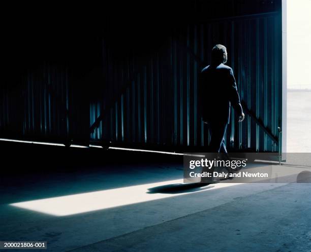 man walking in light from open warehouse door - dark warehouse stock pictures, royalty-free photos & images